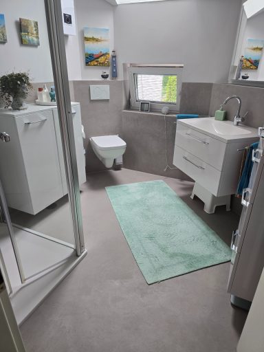 Nach der Modernes Badezimmer in Betonoptik, Fugenlos. Helles Badezimmer mit Dusche, Waschbecken, WC und einem grünen Teppich.